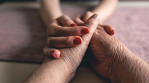 Two hands holding gently. A younger hand with red nail polish rests on an older hand in support.
