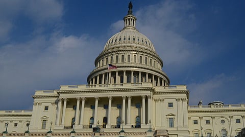 The image shows the U.S. Capitol Building with its iconic dome under a clear blue sky.