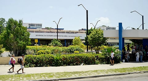 A Cuban hospital with some people walking in front of it.