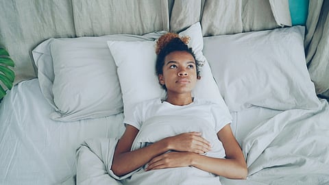 Woman lying awake in bed with white sheets, looking upwards thoughtfully. 