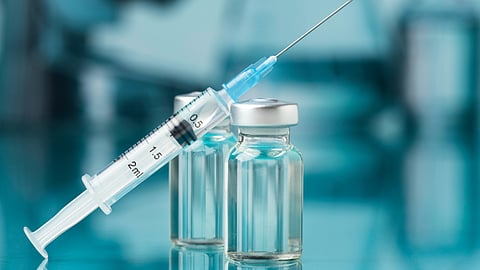 Syringe filled with liquid rests atop two clear, capped vials.