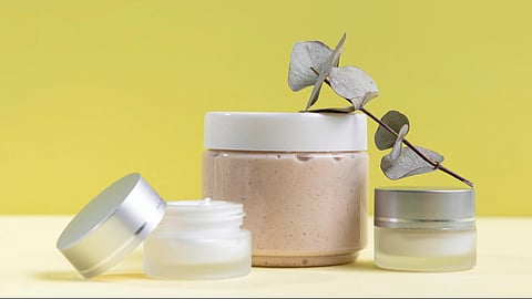 Three cosmetic jars, one open, on a yellow background.