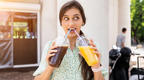 Young woman sipping two drinks, one iced coffee, the other orange juice, through straws.