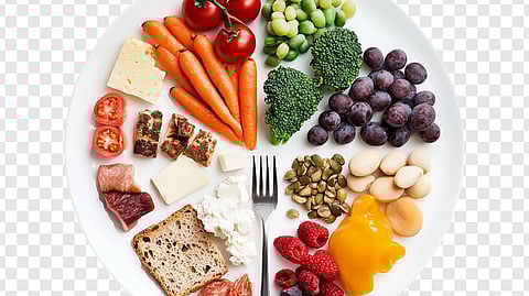 A white plate with a balanced variety of colorful foods, including tomatoes, carrots, broccoli, grapes, cheese, bread, seeds, and bell pepper