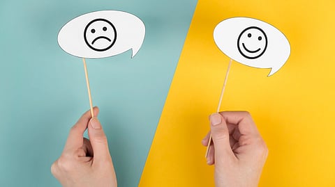 Two hands hold speech bubbles: left, a sad face on a teal background; right, a happy face on a yellow background.
