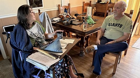 A woman in a wheelchair chats with a man in a "Giants" shirt across a table. 