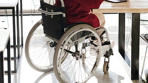 A woman in a marron sweater and white shoes sitting on a wheel chair.