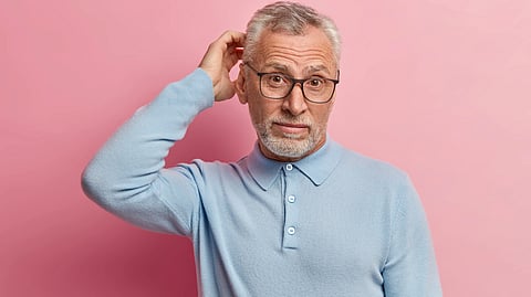 Senior man wearing glasses and a sweater, posed against a pink background.