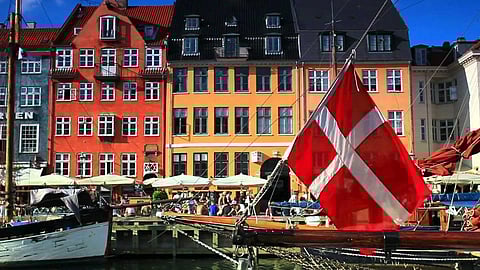 Denmark with its colorful building in the background and a boat jetty with one boat with Denmark flag. 