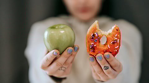 A blurred woman holds a green apple in one hand and donut in another hand.