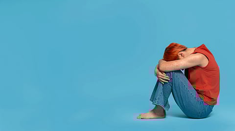 A sad person sitting curled up with head down.