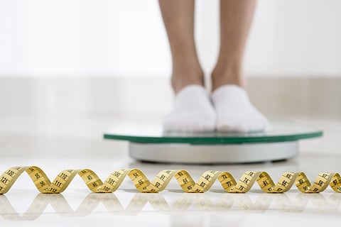A person standing on a weighing scale and a measuring tape lying nearby.