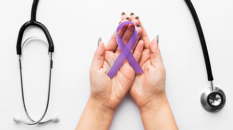 Hands gently hold a purple awareness ribbon, a stethoscope beside them on a white background.