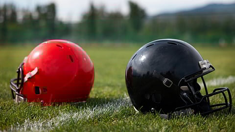 Two football helmets, one red and one black, rest on a grassy field. 