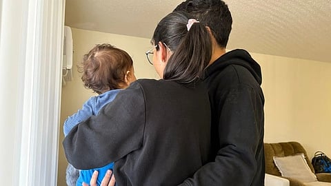 A family standing together in a living room, viewed from behind. 