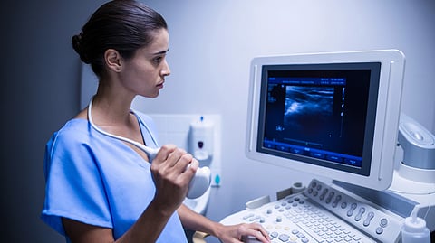 A focused medical professional in blue scrubs operates ultrasound equipment.
