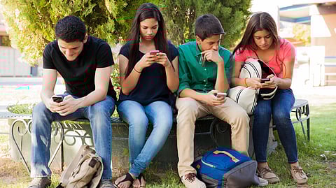 Group of teenage boys and girls ignoring each other while using their cell phones sitting under a tree.