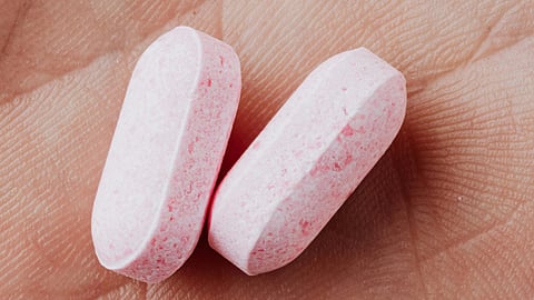 Two pink tablets rest in a person's palm.