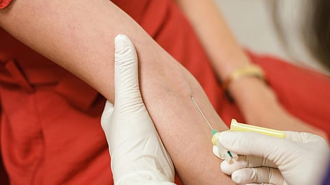A healthcare professional in gloves administers a vaccine or draws blood from a person's arm in a red dress.