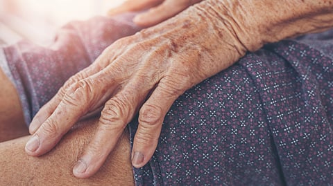 Close-up of an elderly person's hand resting on their knee, showcasing wrinkles and age spots. 