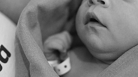 A baby with hospital band in black and white.