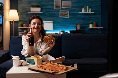 Happy woman holding beer bottle eating tasty takeaway food delivery.