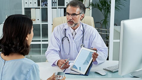Doctor in a white coat and stethoscope discusses information on a tablet with a patient in an hospital room.