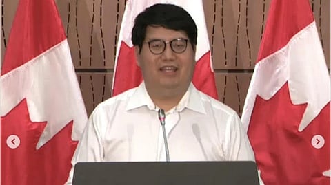 Dr. David Poon speaking at an event with Canada flags behind. 