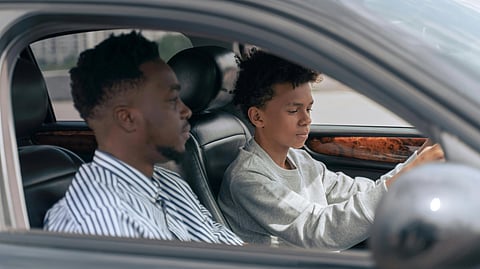 A young person intently focuses on driving a car, with an adult supervising in the passenger seat. 