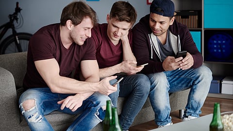 Three friends sit on a couch, looking intently at a smartphone.