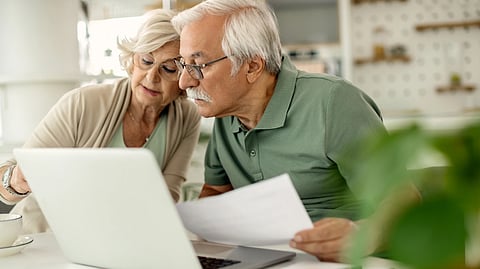 Elderly couple focused on a laptop screen, reviewing documents at a cozy kitchen table. 