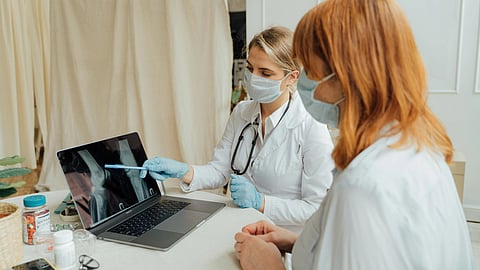 A doctor and patient, both wearing masks, discuss an X-ray on a laptop at a clinic. 