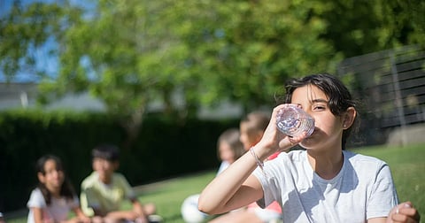 Child drinking water outdoors in summer sunlight to stay hydrated and prevent heat exhaustion