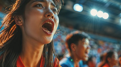 An excited fan in red cheers loudly in a crowded stadium during a game.