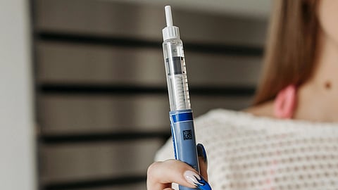 A person holds a syringe pen against a striped background.