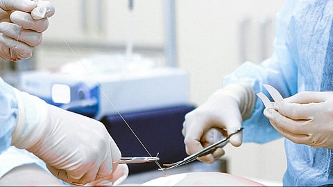 2 sets of hands during on going surgery, holding medical equipment.