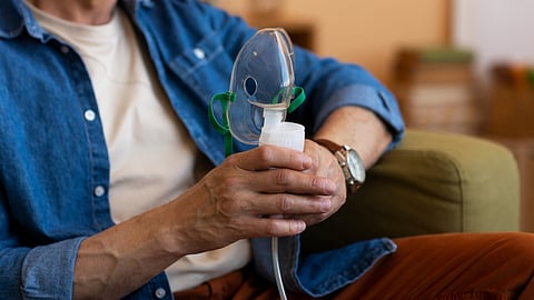 A person holds an oxygen mask while seated on a couch.