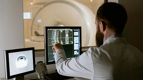A medical professional analyzes CT scans on dual monitors.