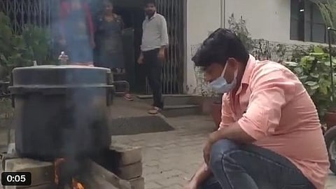 A man in pink shirt cooking on a woodfired makeshift kitchen.
