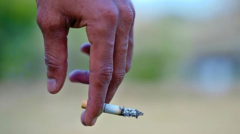A hand holding a lit cigarette with ash forming at the tip. 