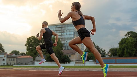 Two athletes, a man and a woman, sprint on a track at sunset. 
