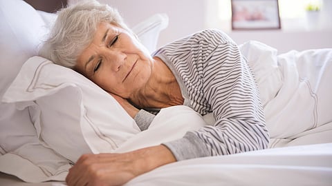 Elderly woman peacefully sleeping on her side, resting her head on a pillow, wearing a striped shirt.