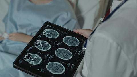 A doctor holding brain scans and patient on hospital bed.