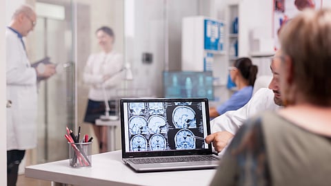 Doctor discusses brain scans on a laptop with a patient in a modern medical office. 