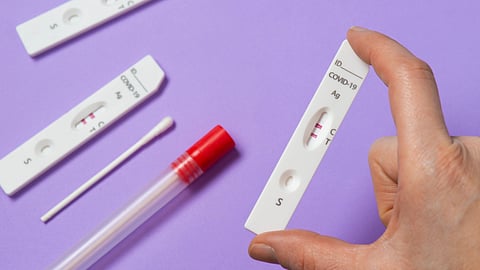 A hand holds a COVID-19 rapid test cassette showing two pink lines.