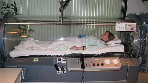 A woman is lying down in a hyperbaric chamber for therapy.