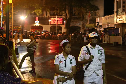 Two healthcare providers walking on a street illuminated by light during night hours.