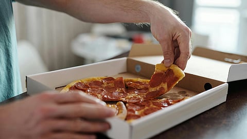 A person in a teal shirt is taking a slice of pepperoni pizza from an open pizza box