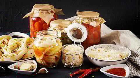 An arrangement of jars filled with pickled vegetables, a white bowl with sauerkraut, and dishes with spices and chili sauce.