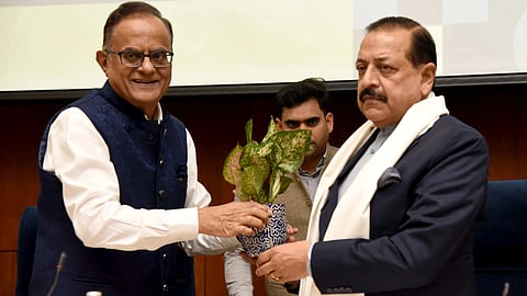 Two men exchange a potted plant, Dr. Jitendra Singh smiles warmly while the other looks serious.